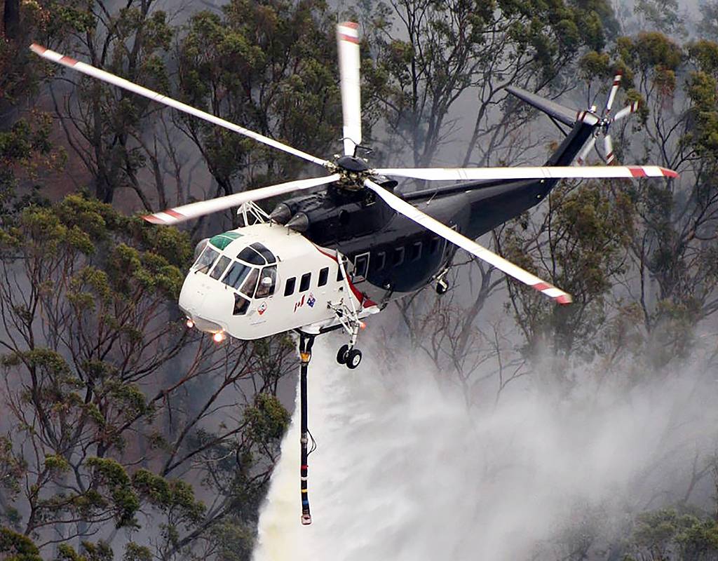 A Sikorsky S-61 helicopter performs a water drop during an aerial firefighting mission. WinAir Photo