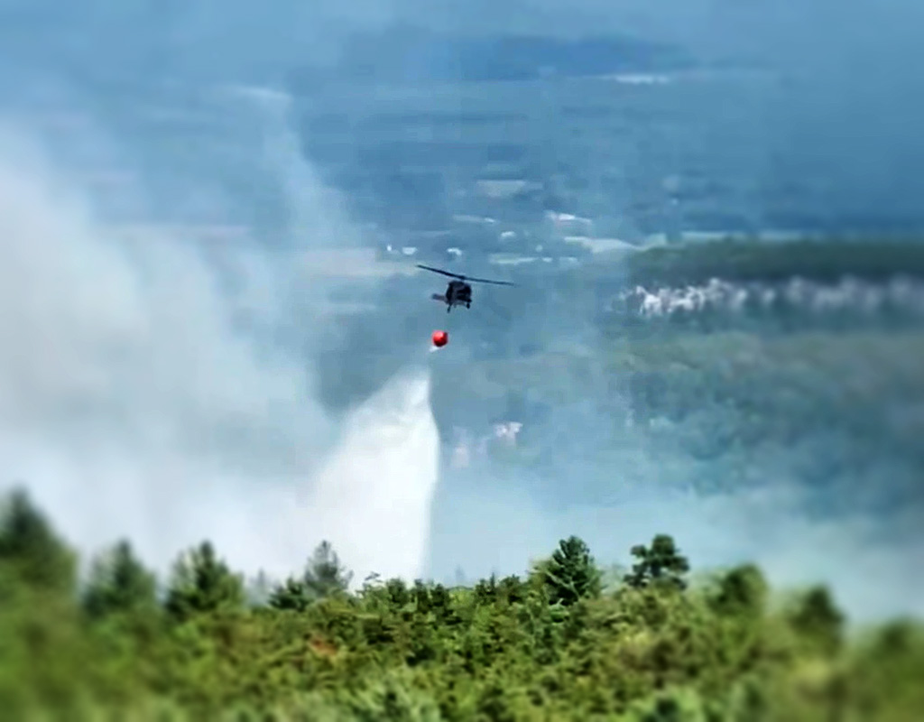 A New York Army National Guard UH-60M Black Hawk helicopter drops 600 gallons of water on a wild fire raging along a ridgeline in Minnewaska State Park Preserve in the Hudson Valley near Ellenville, New York on August 30, 2022. U.S. Army National Guard photo courtesy New York National Guard State Aviation Office