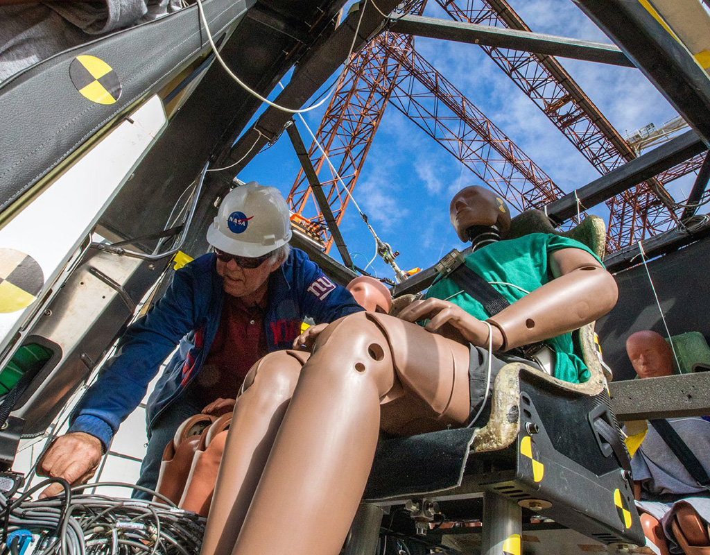 A NASA researcher assists in the preparation of a crash test dummy seated inside a lift-plus-cruise model eVTOL. Researchers use crash test dummies to learn how the crash impact would affect humans. Image courtesy of Dave Bowman