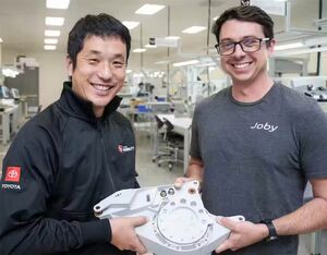 Kazuhiro Sato (left) and Jordin Gischler (right) present a completed tilt actuator, manufactured at Joby’s San Carlos production facility with key parts supplied by Toyota. Joby Aviation Photo
