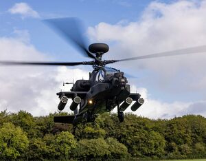 An Apache AH-64E helicopter hovers in front of a woodblock. British Army Photo